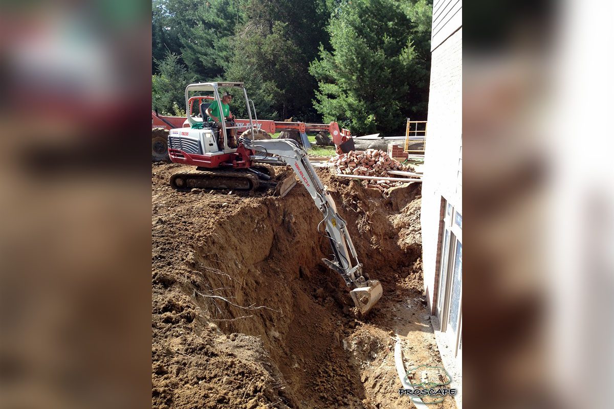 0_0003_lanscape-2 copy Mini excavator digging near a building foundation.
