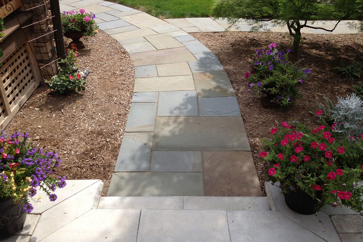 Curved stone pathway with colorful potted flowers.