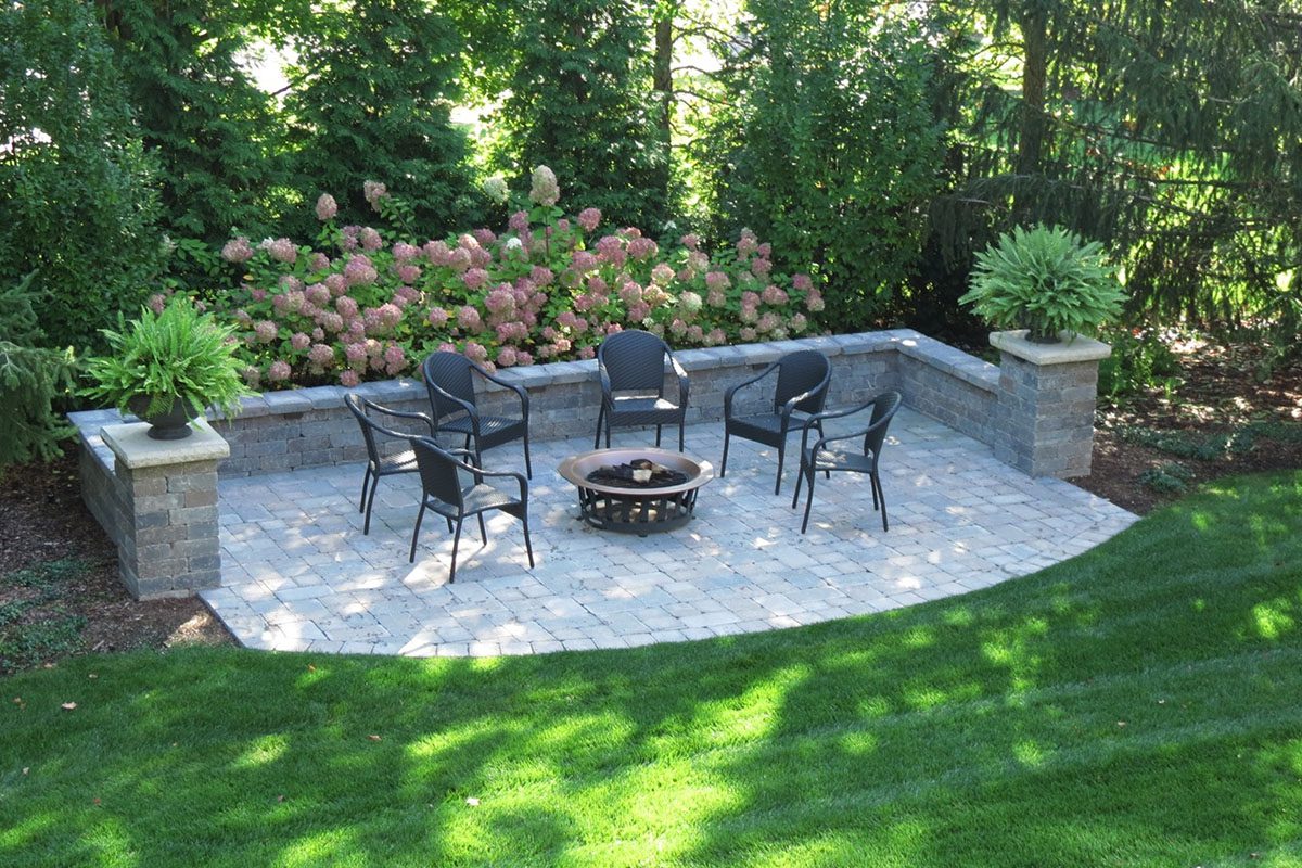 Patio with chairs and fire pit, garden backdrop.