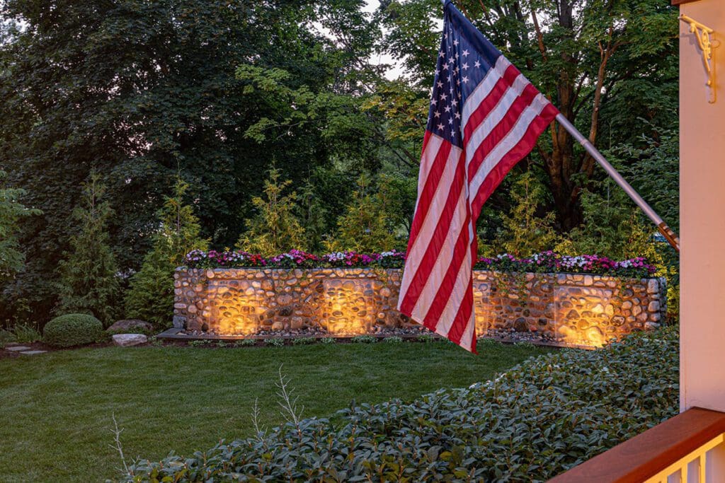 American flag near illuminated garden wall.