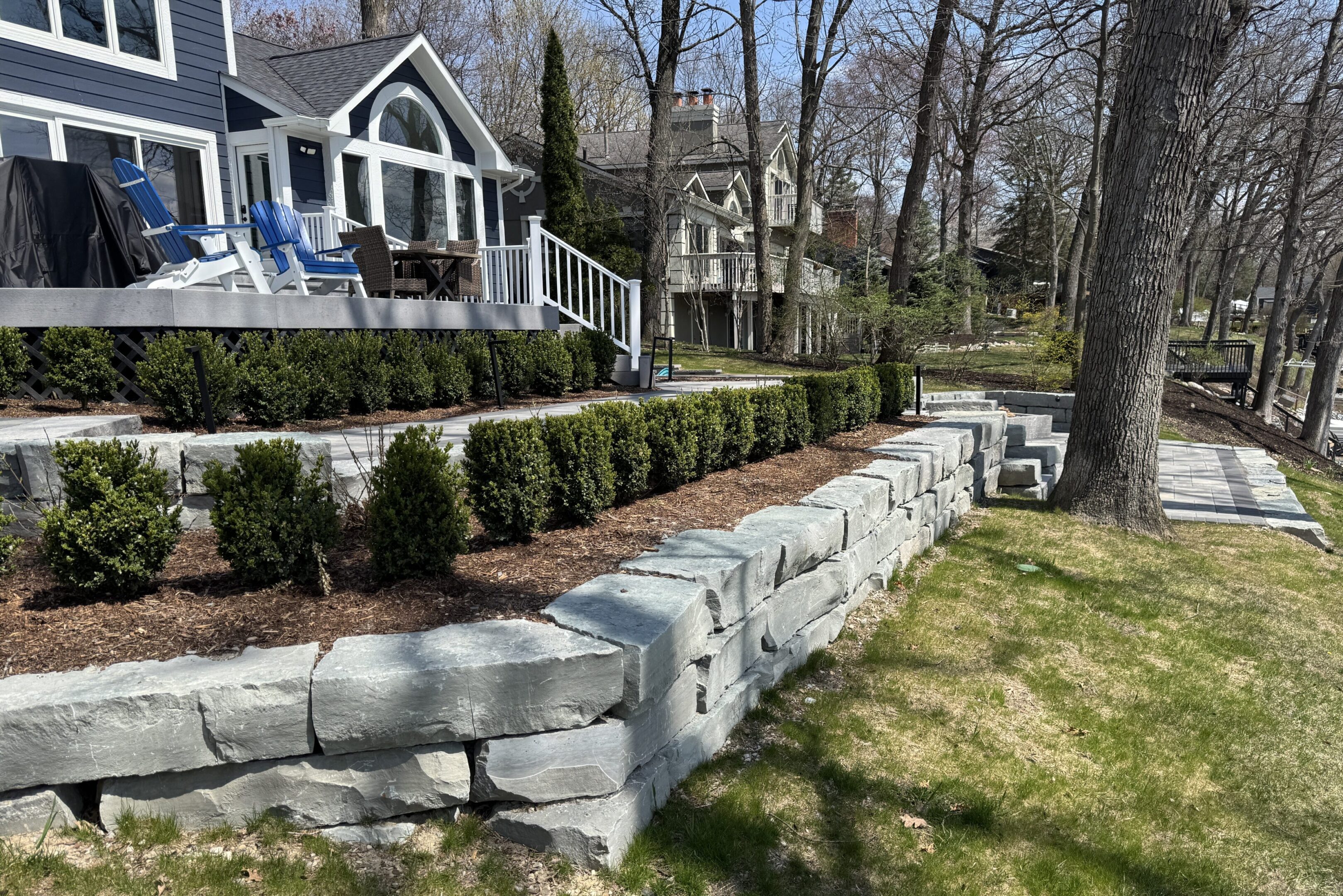 A stone wall with bushes and trees in the background.